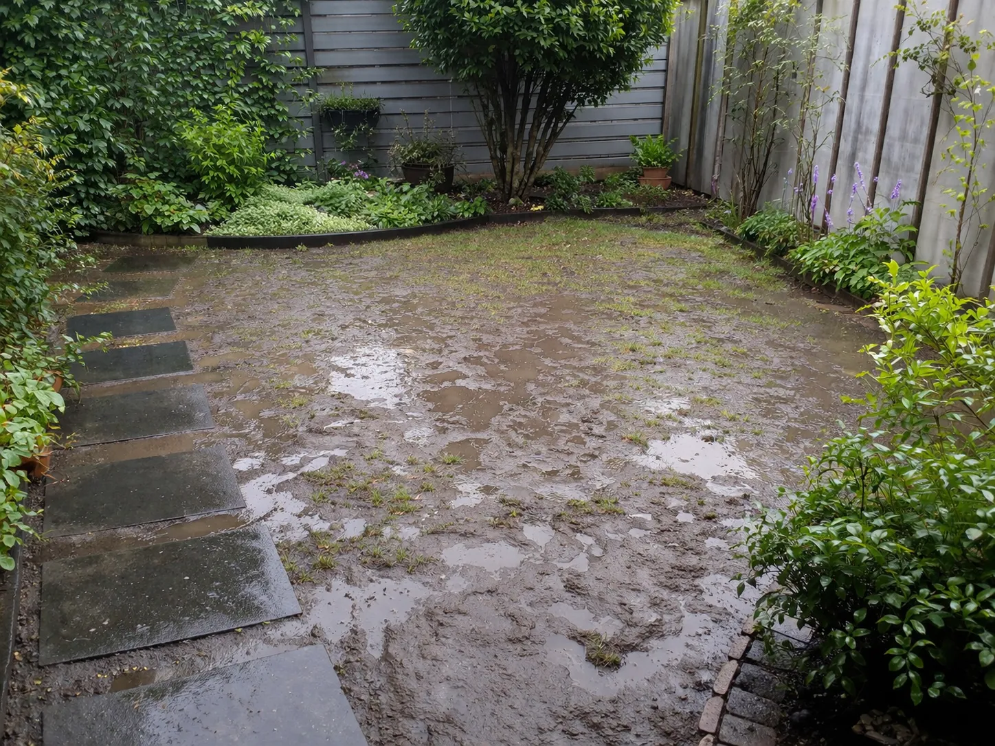 Natte achtertuin met plassen en modder na regen. Realistische foto zonder tekst in beeld.