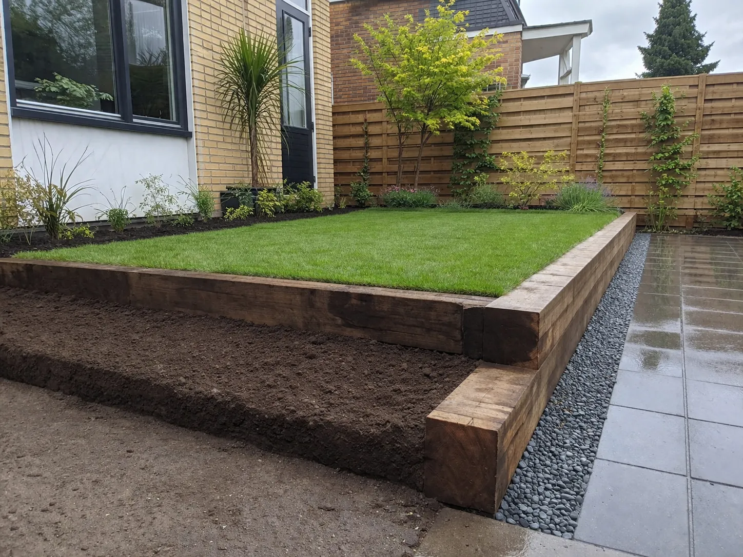 Verhoogde tuin met gras, planten en goede afwatering tegen regenwater.