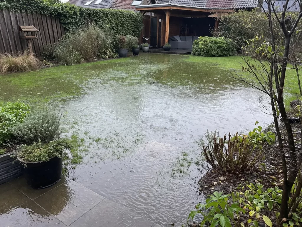 Een realistische foto van een tuin met grote plassen en stilstaand regenwater na een flinke bui.