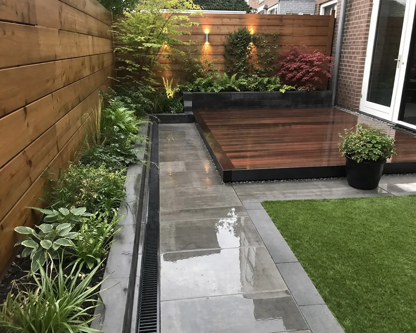 Kleine tuin met slimme afwatering, verhoogde plantenbakken en waterdoorlatende bestrating.